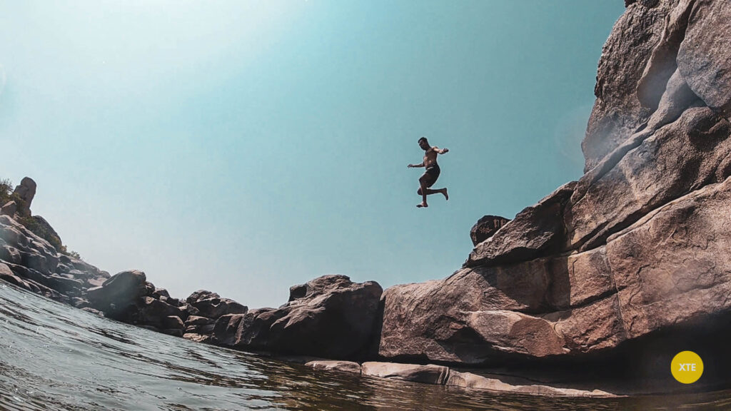 A person jumping off a cliff at a pond near Hampi Waterfall