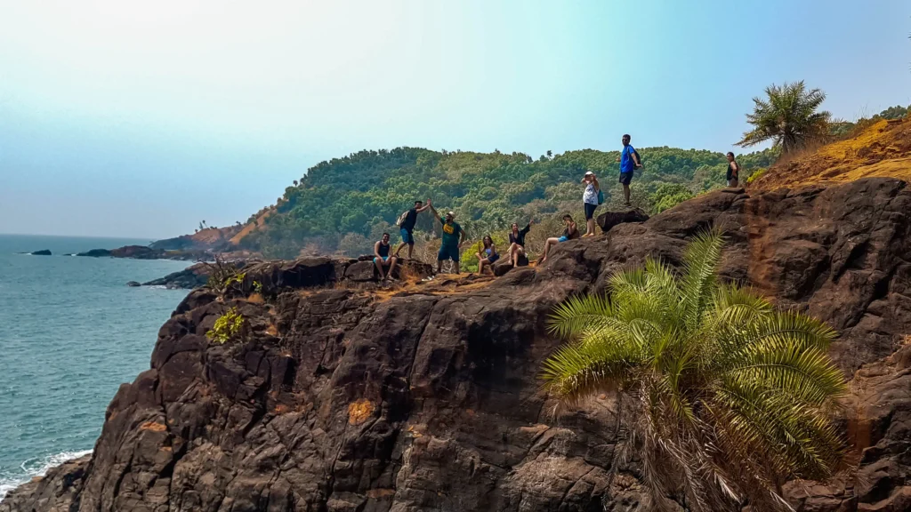 group of people sitting atop a cliff near the ocean in gokarna while doing the bech trek