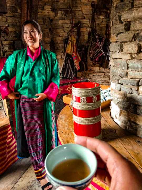 Bhutanese woman in Kira traditonal dress serving local wine showing Happiness and content